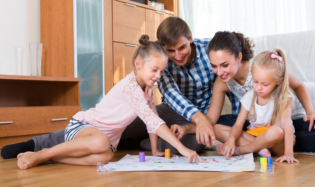 Happy young parents and two little daughters playing a board game at home represent how Lake Forest family law attorneys can help.