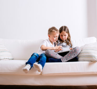 A little girl and boy sit on a sofa with a tablet looking at their mother's Chicago divorce attorneys' website.