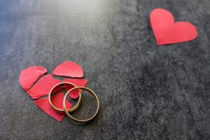 Wedding rings and broken red  heart. Black background. The concept of divorce, parting, infidelity. Selective focus.