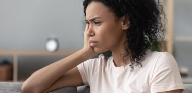 A women sitting on a gray couch looking worried, representing how one can benefit from calling a Chicago divorce lawyer.