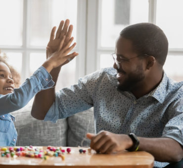 A father and daughter playing a board game and high fiving each other with big smiles, representing how one can benefit from calling a Chicago child support lawyer.