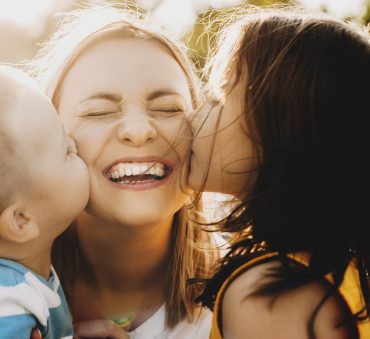 A woman smiling getting kisses by her children, representing how one can benefit from calling a Chicago divorce attorney.