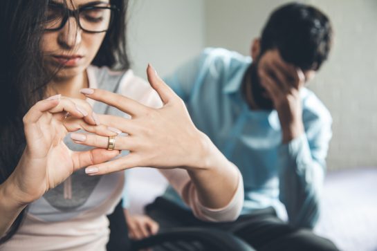An upset woman taking off her wedding band in the foreground with an sad man in the background, representing how our Lincoln Park divorce attorneys can represent you in your divorce case.