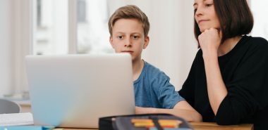 A teen boy working virtually on laptop with his mother beside him, to develop a child custody agreement consult with Chicago Parenting Plan Attorney.