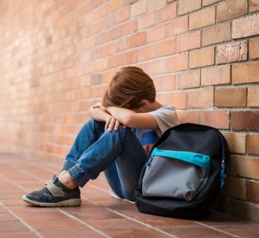Sad young boy sitting on corridor with hands on knees and head between his legs because his parents got a divorce. Parents divorced with Chicago divorce attorney and learn about how the divorce will affect their child.