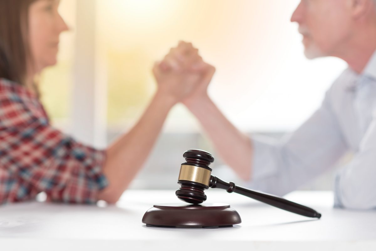 A man and woman are sitting behind a gavel and their hands are interlocked as if they may arm wrestle. Chicago divorce attorney suggests ways to help turn that animosity into a constructive way of working together to benefit the kids and divorce long term.