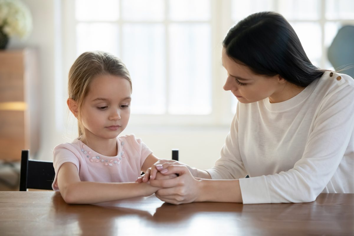 A mother is holding her young daughter's hands at the table and really focusing on the girl's emotions through the divorce as suggested by Chicago divorce attorney.